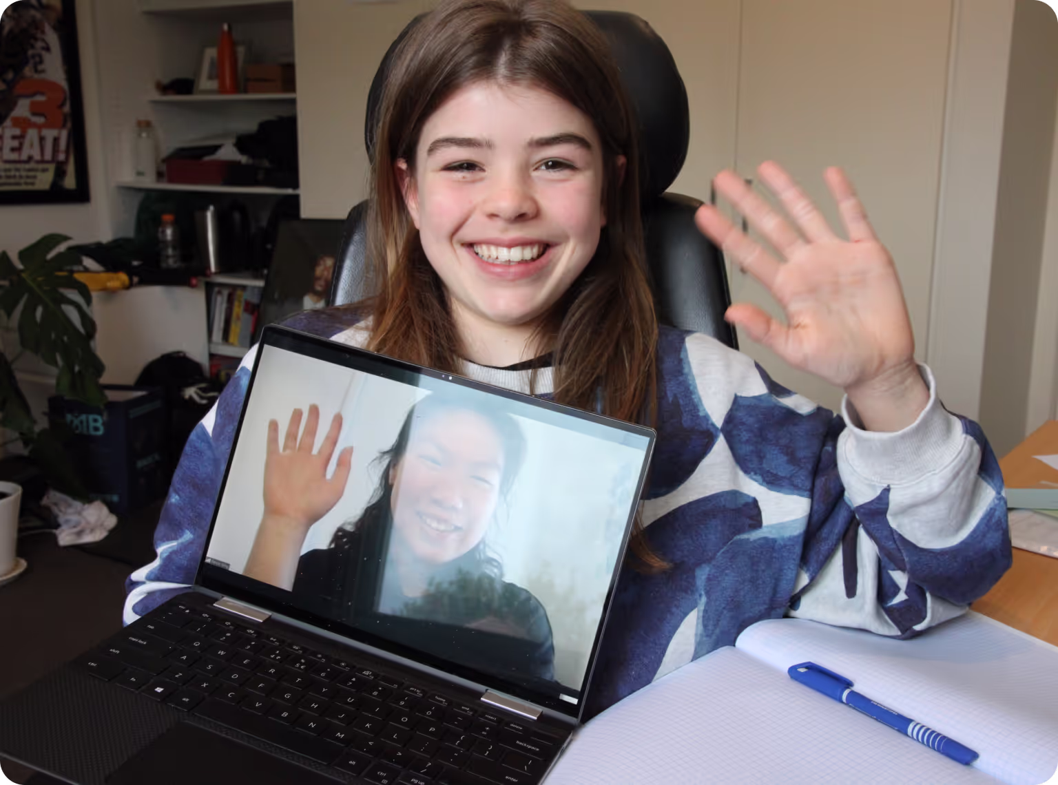 A smiling student waving hello to their online teacher on a laptop